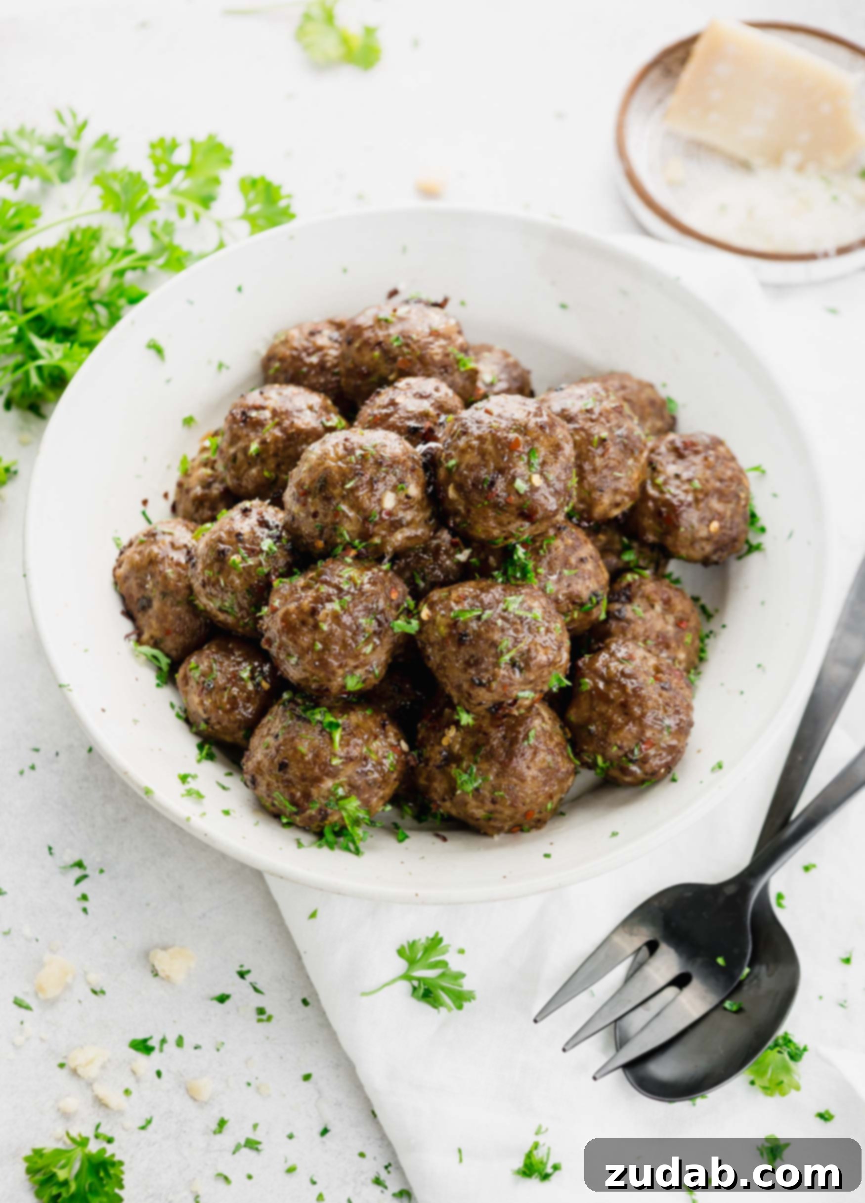 Melt in Your Mouth Meatball Recipe A rustic bowl filled with perfectly browned meatballs, lightly garnished with fresh basil. Two forks are positioned beside the bowl, ready for serving.