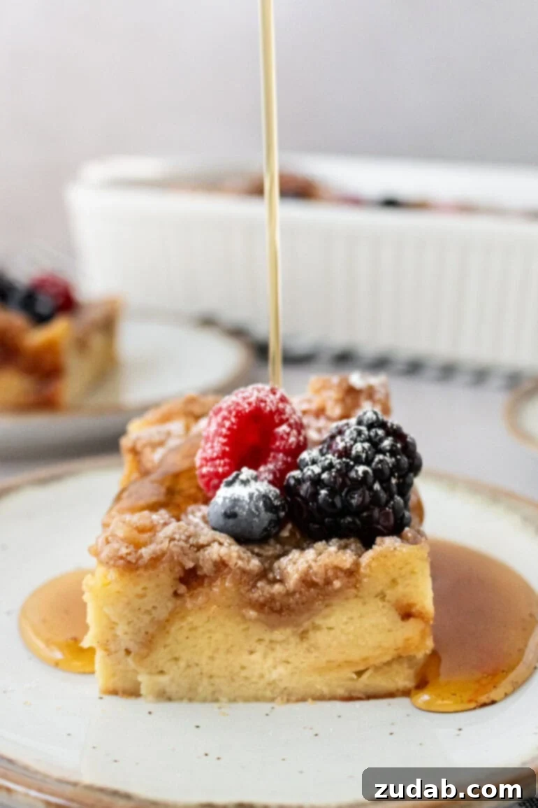 Someone pouring syrup generously over a piece of French toast casserole topped with fresh berries.