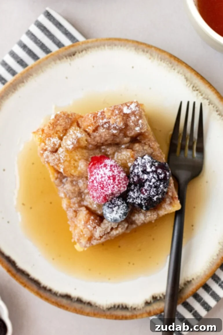 An overhead shot of a piece of French toast casserole, beautifully topped with fresh berries and powdered sugar, resting in a pool of syrup.