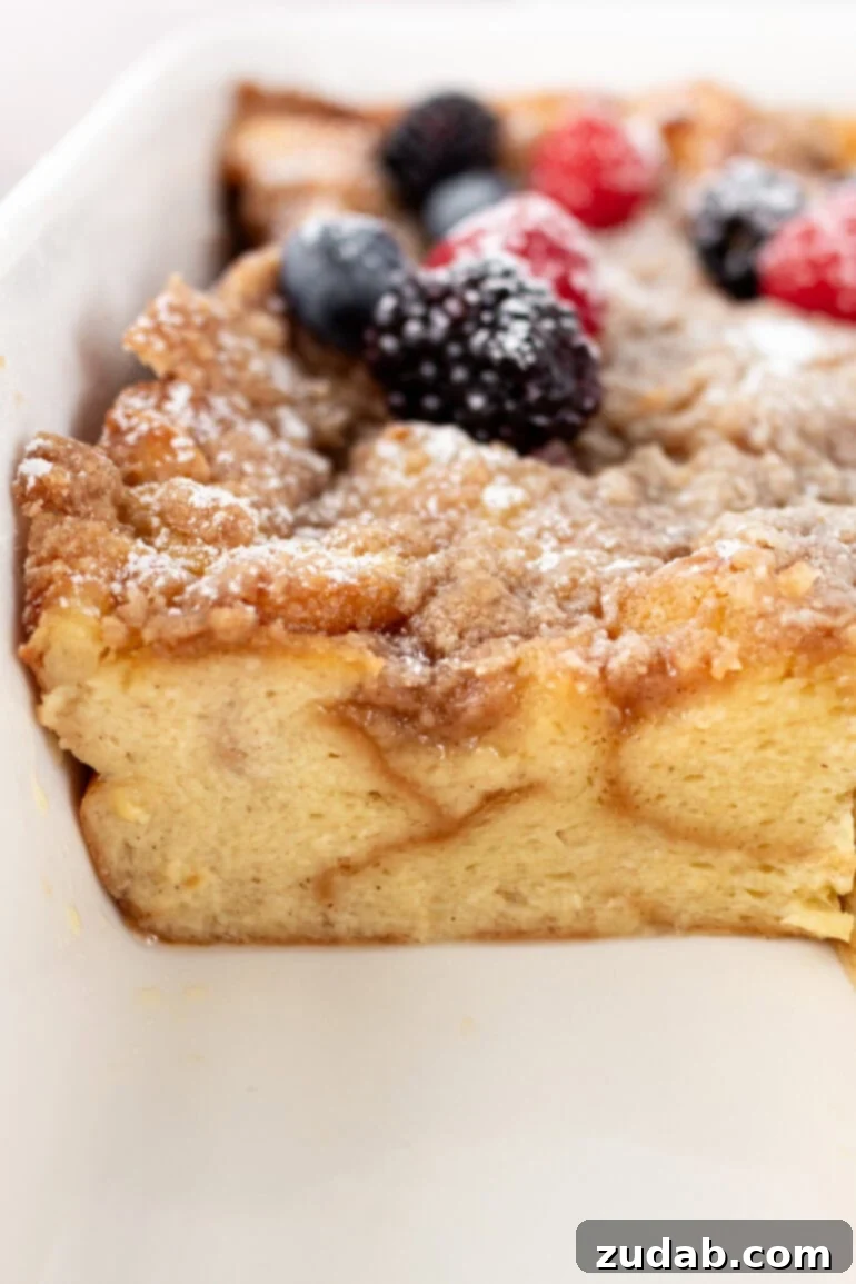 A serving of French toast casserole, elegantly topped with powdered sugar and a vibrant medley of fresh berries, removed from a full baking pan.