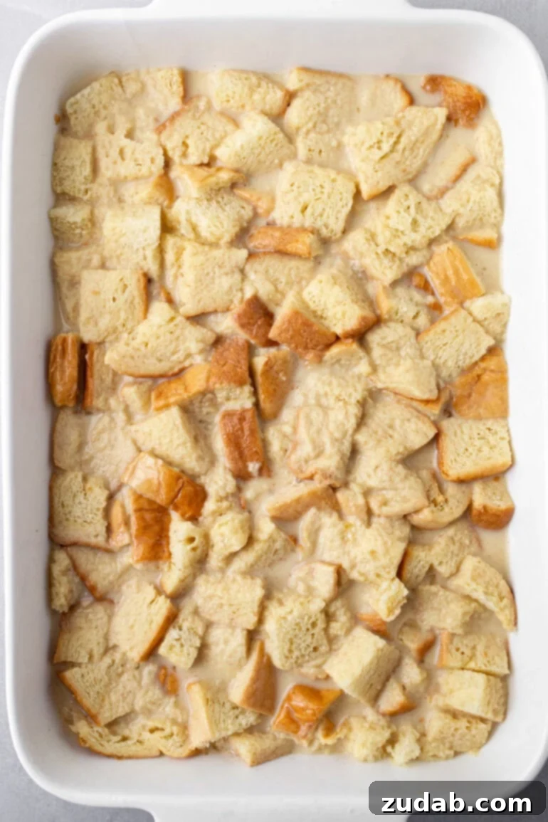 A closer view of the French toast casserole custard mixture being poured over cubed bread.