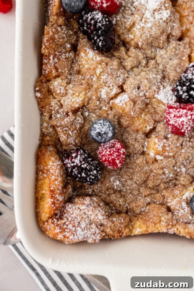 An overhead view of a baked French toast casserole, featuring a delicious streusel topping, fresh berries, and a dusting of powdered sugar.
