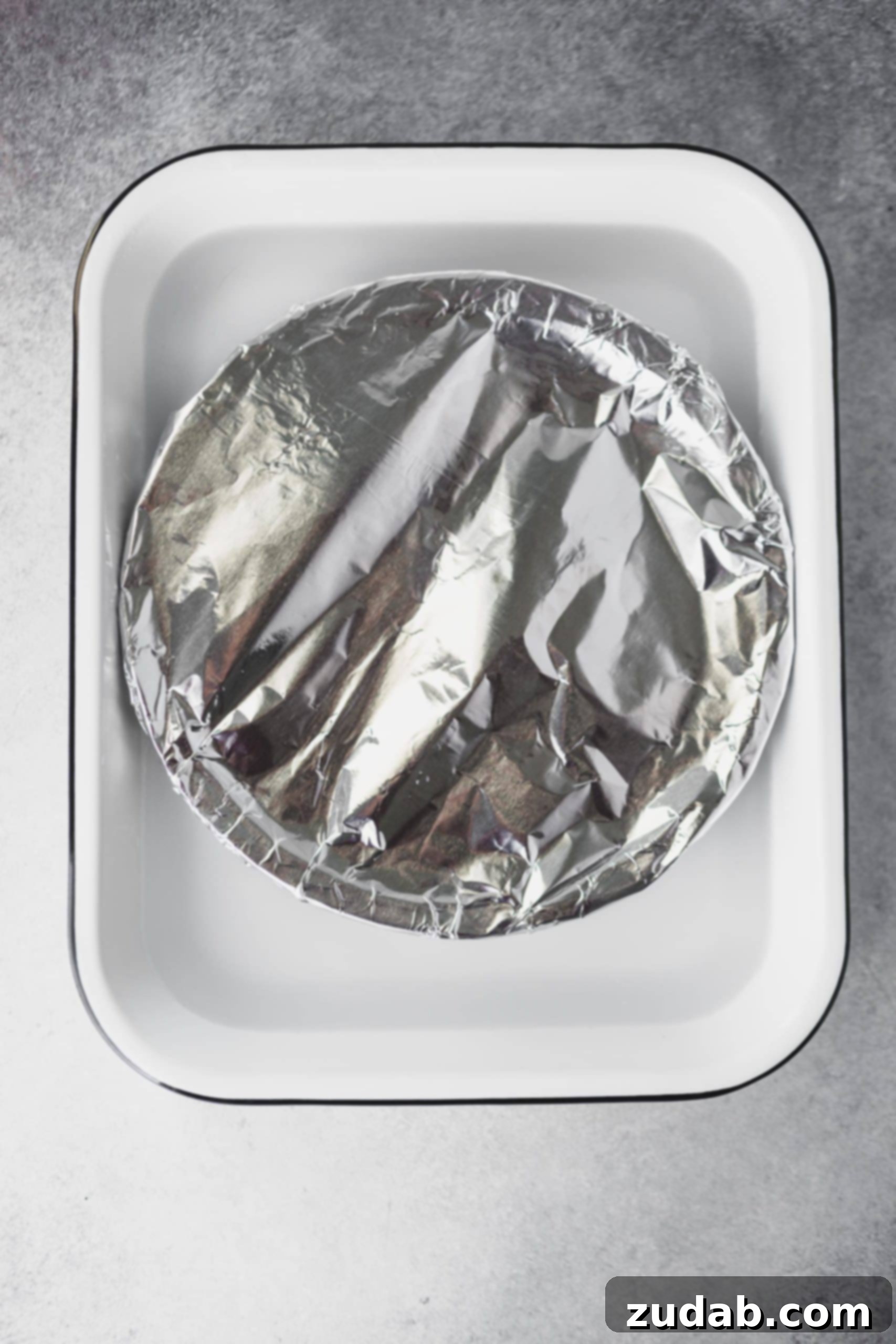 Homemade Dulce De Leche Recipe A glass pie plate, tightly covered with aluminum foil, resting in a larger casserole dish filled with an inch of water, ready for oven baking.