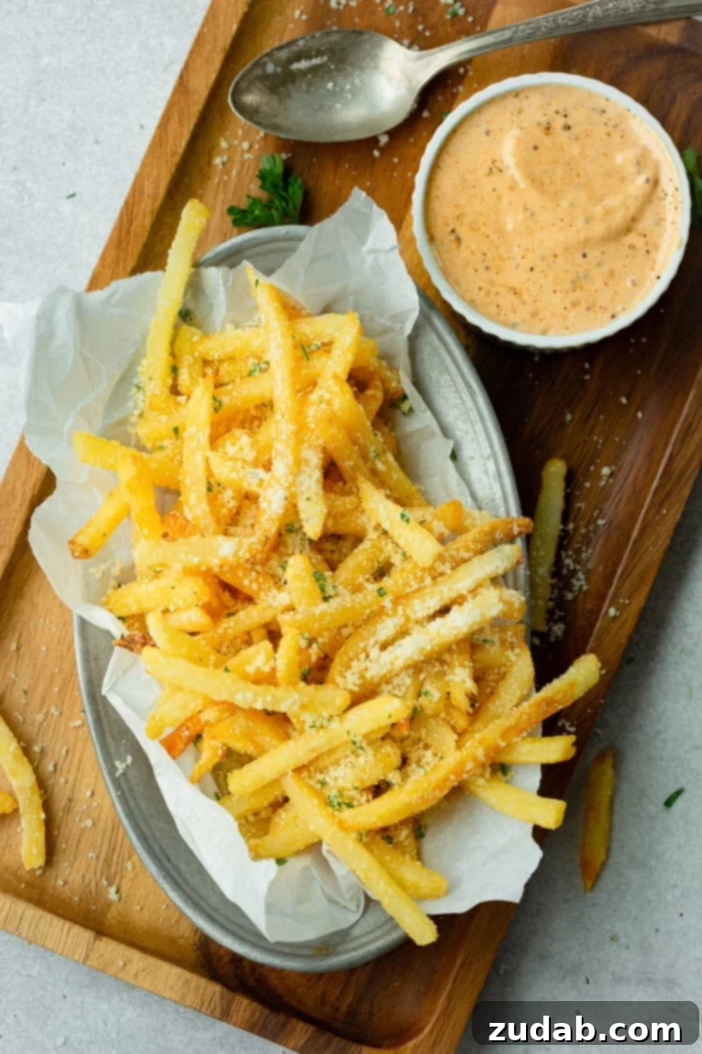 Disneyland's Iconic French Fry Recipe 2 A dish full of hot, salty parmesan fries with a ramekin of vibrant Cajun remoulade dipping sauce beside it.
