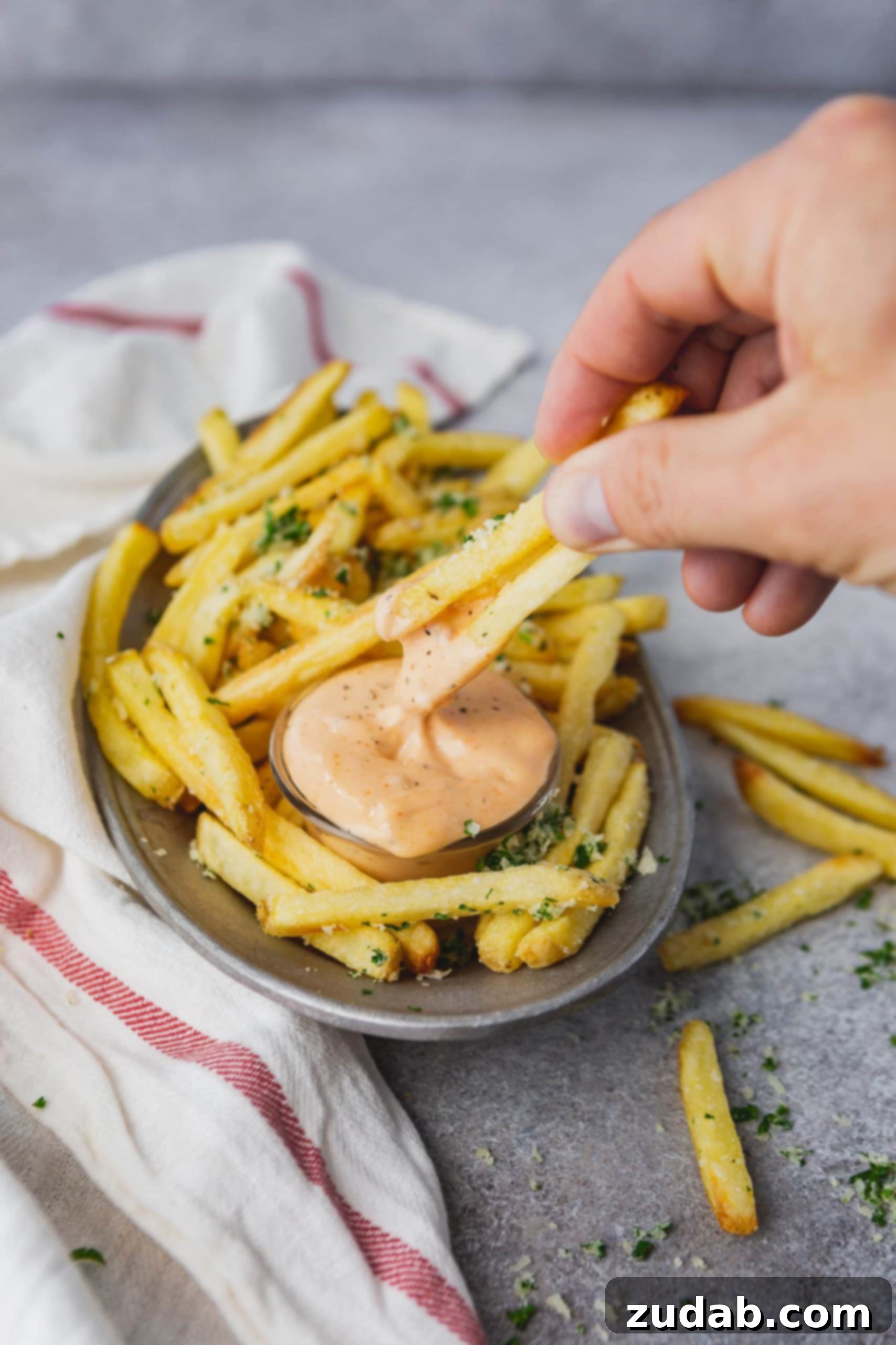 Disneyland's Pomme Frites Dipping Sauce Cajun Remoulade A plate of golden pomme frites with a small cup of Cajun dipping sauce, and a hand dipping two fries into the sauce.