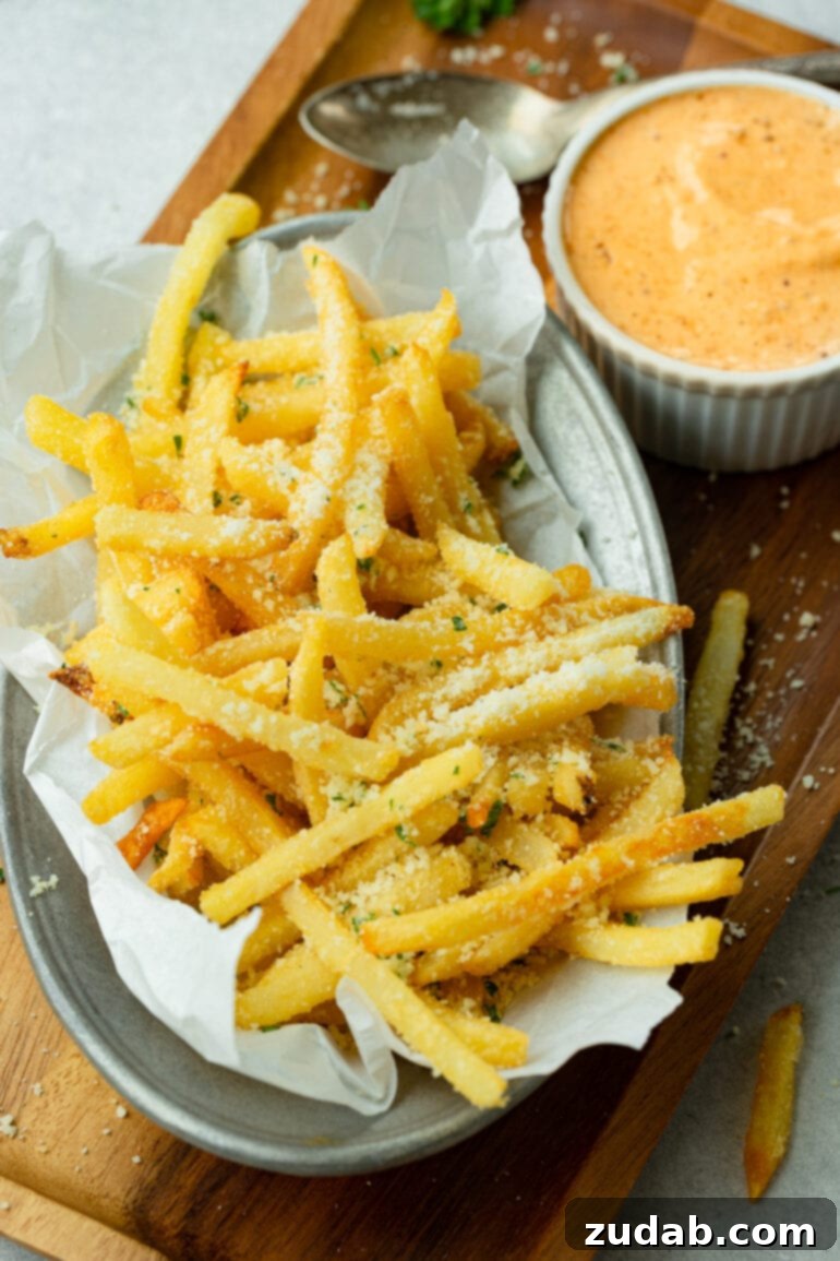 Disneyland's Iconic French Fry Recipe 6 A photo of a plate laden with hot, salty pomme frites generously covered in Parmesan cheese, next to a small bowl of Cajun dipping sauce.