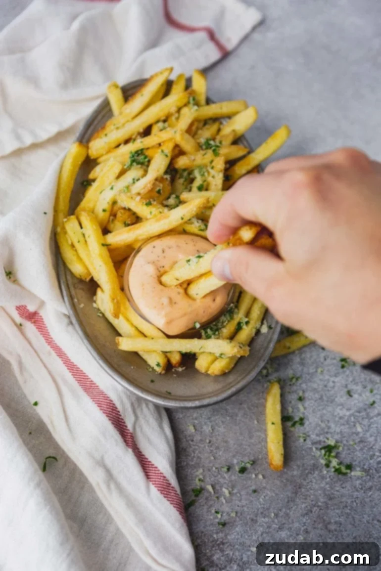 Disneyland's Iconic French Fry Recipe 7 A photo of a plate of golden pomme frites with a cup of Cajun dipping sauce, featuring someone dipping two fries into the sauce.
