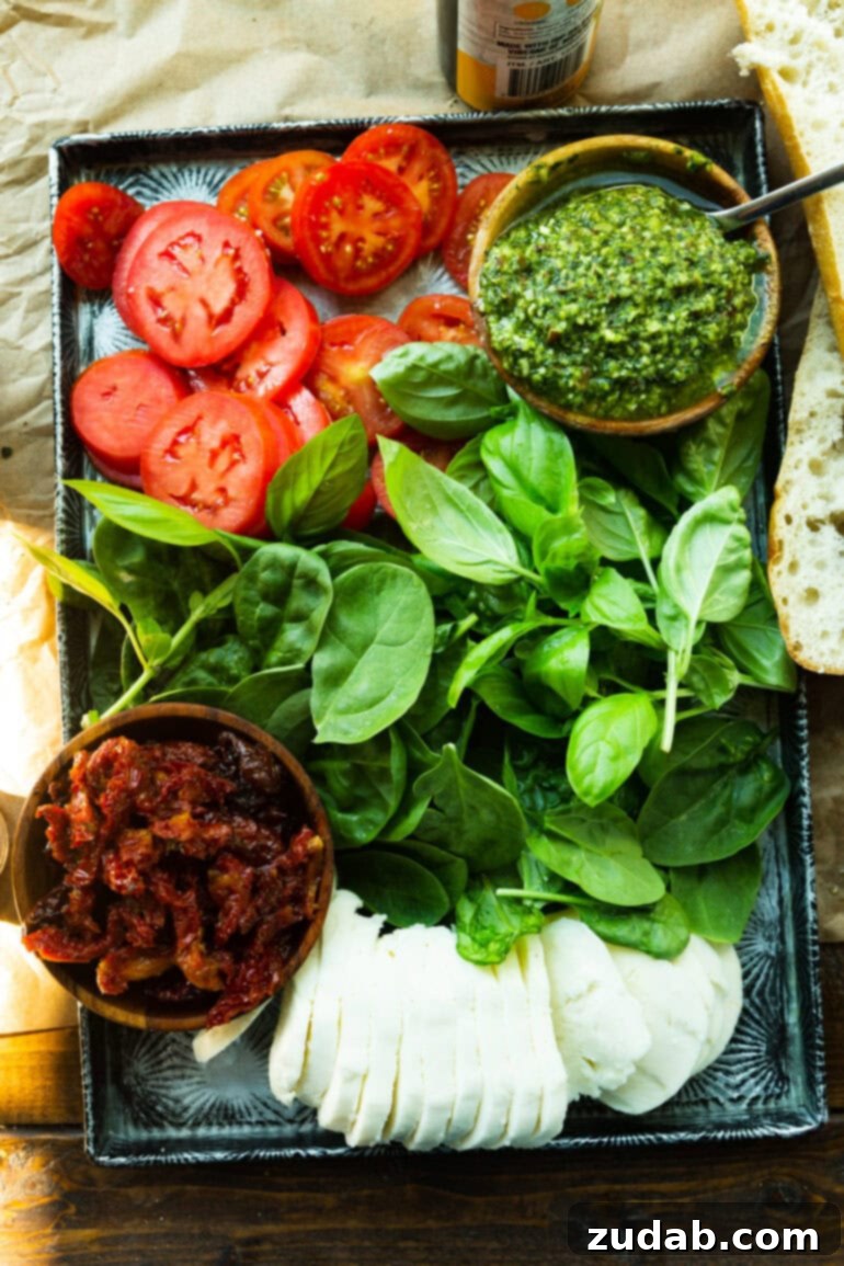 Italian Panini 3 A photo of all the layers needed for an Italian pressed sandwich including fresh spinach, sun-dried tomatoes, pesto, sliced tomatoes, and mozzarella cheese