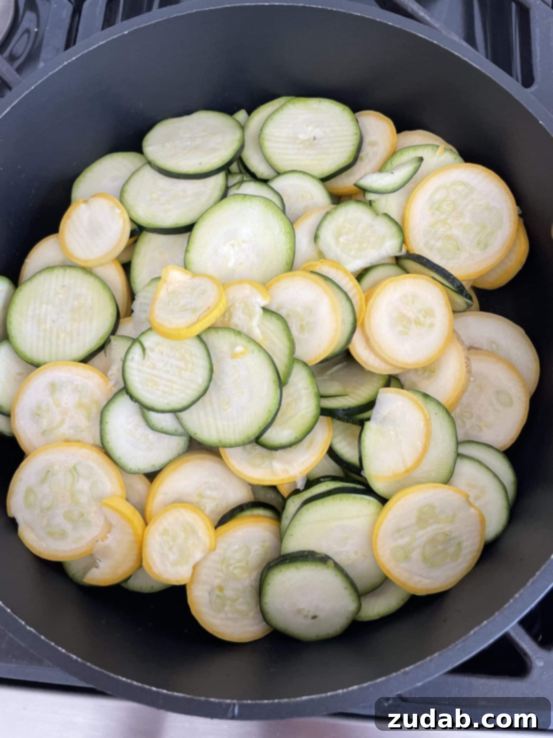 A cast iron skillet filled with thinly sliced zucchini and yellow squash, creating a colorful and fresh base for the gratin.