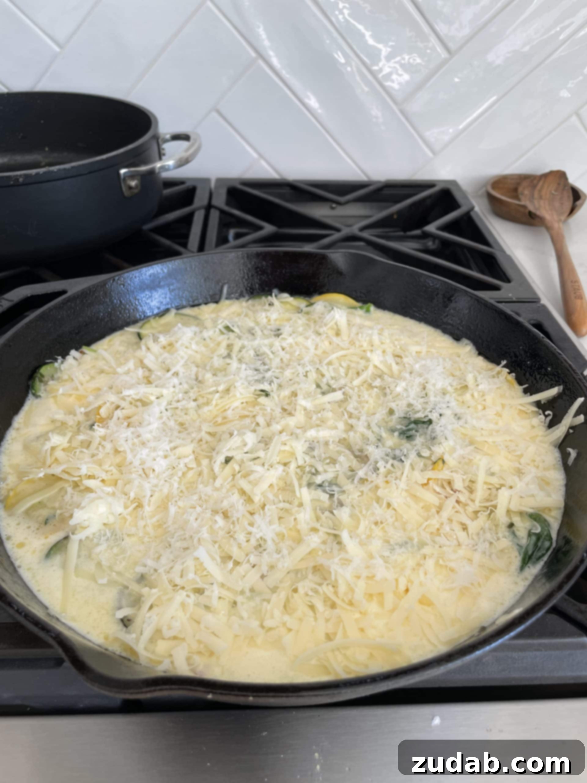 A rich egg and cream mixture being poured over a bed of sautéed zucchini, yellow squash, and spinach in a cast iron skillet, ready for its cheesy topping.