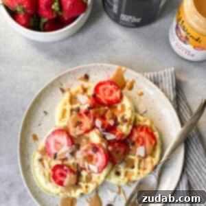 A photo of three small circular waffles topped with sliced strawberries on a white plate with a fork sitting on the side of the plate