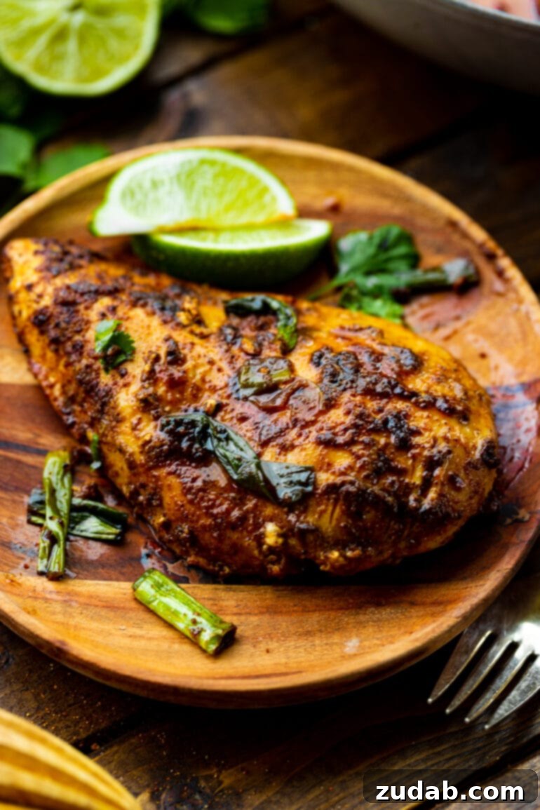 Easy One-Pan 10-Minute Sticky Mexican Chicken 7 A beautifully pan-seared chicken breast, covered in a rich Mexican rub, artfully presented on a rustic wooden plate with two fresh, zesty lime wedges resting beside it.