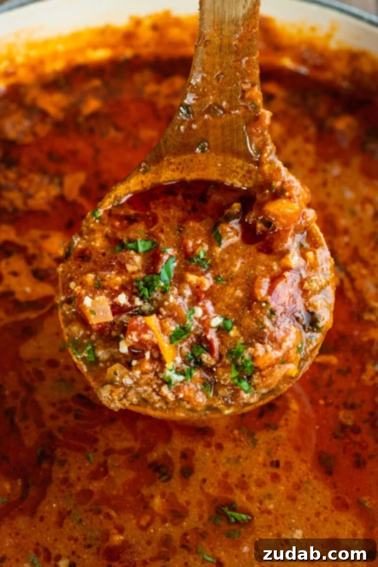 Rustic Italian Beef Chili 3 A wooden spoon lifting a generous scoop of steaming chili out of a large cooking pot, showcasing the rich texture and vibrant colors of the dish.