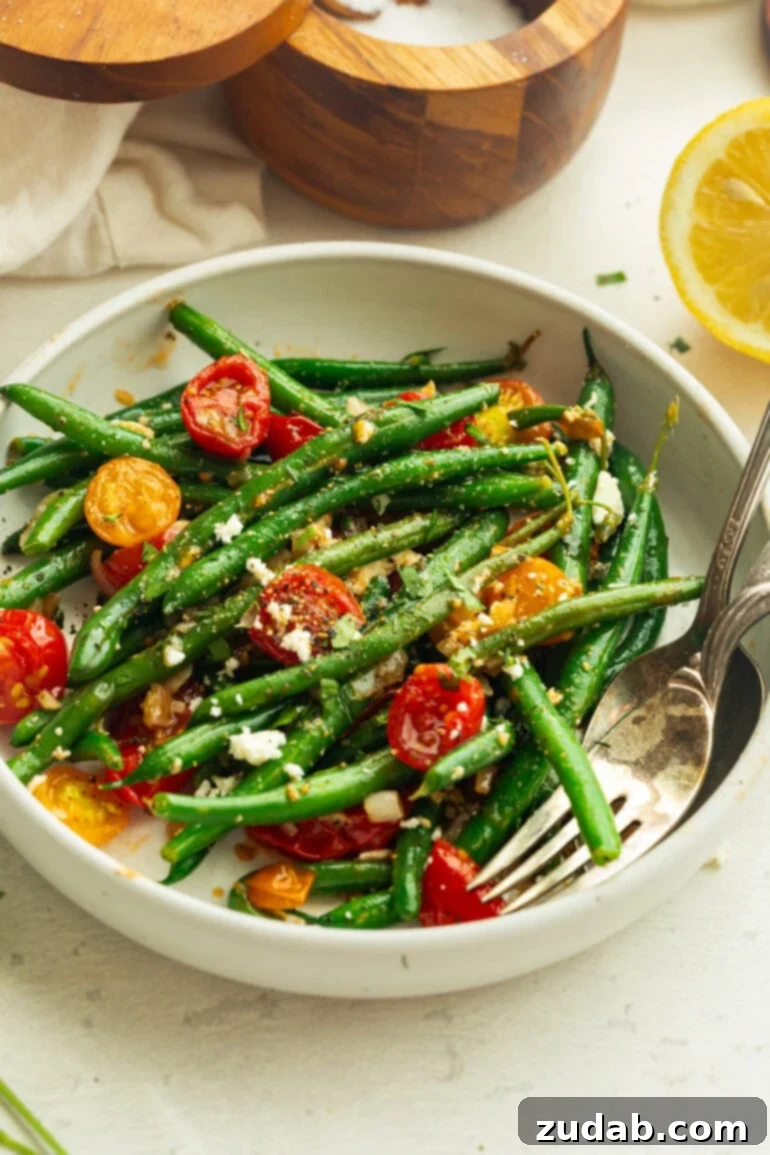 Garlic Green Bean and Cherry Tomato Sauté 2 A close-up of vibrant sautéed green beans and cherry tomatoes in a white bowl, garnished with seasoning and a lemon wedge.