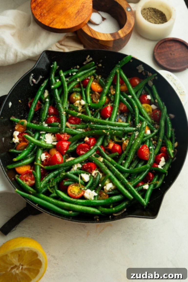 Garlic Green Bean and Cherry Tomato Sauté 5 A cast iron skillet filled with beautifully blistered cherry tomatoes and crisp-tender green beans, generously topped with sliced garlic and fresh herbs, ready to be served.