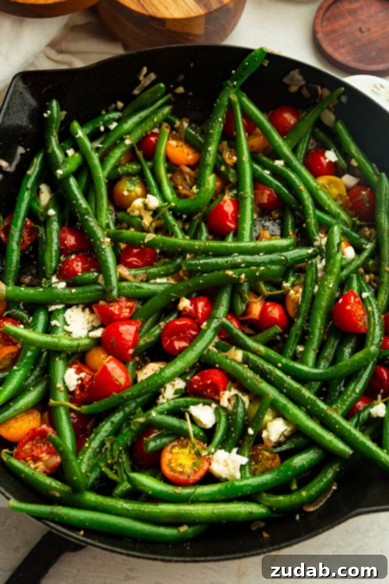 Garlic Green Bean and Cherry Tomato Sauté 6 Bright sautéed green beans and cherry tomatoes in a skillet, garnished with crumbled feta and freshly cracked black pepper, shown from an overhead perspective.