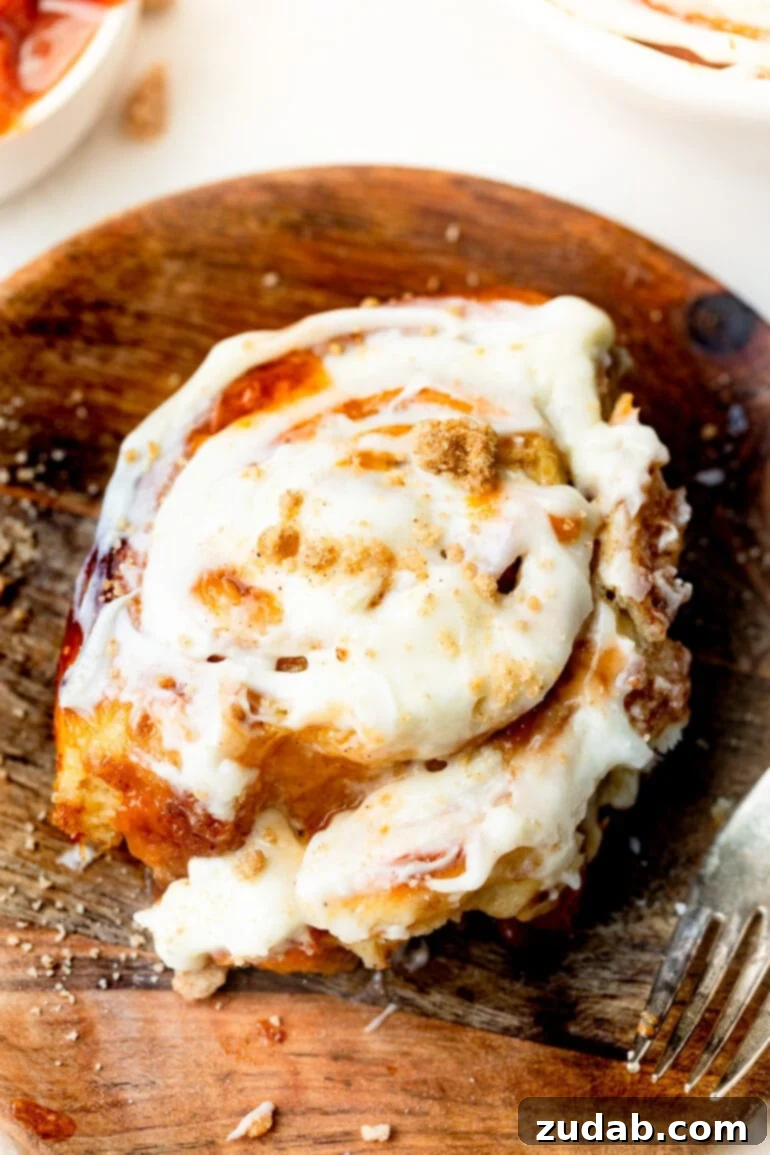 Delicious Peach Cobbler Cinnamon Rolls 2 a photo of a peach cinnamon rolls sitting on a wooden dessert plate loaded with peach jam and topped with peach cream cheese frosting