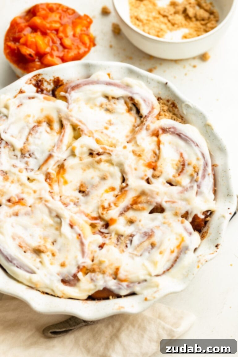 Delicious Peach Cobbler Cinnamon Rolls 11 a photo of a circular baking dish full of baked peach cobbler cinnamon rolls and topped with cream cheese frosting
