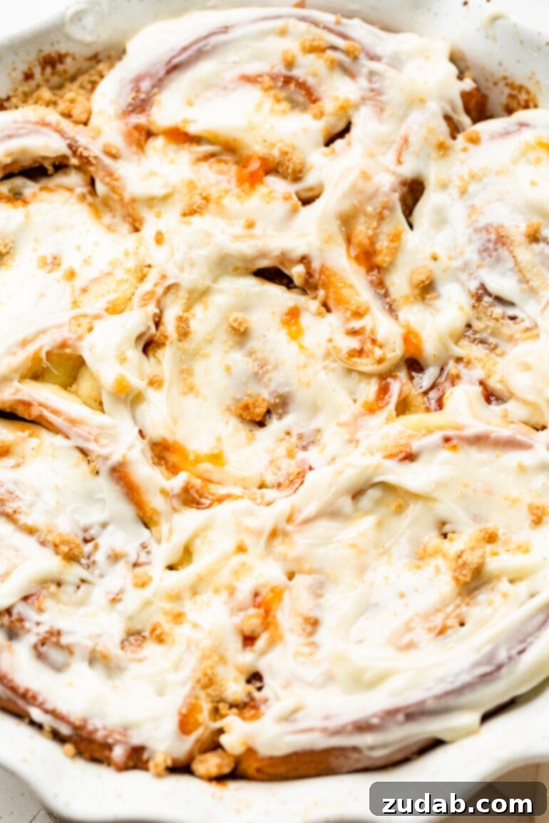 Delicious Peach Cobbler Cinnamon Rolls 12 a photo of a baking dish full of baked peach cinnamon rolls topped with peach cream cheese frosting