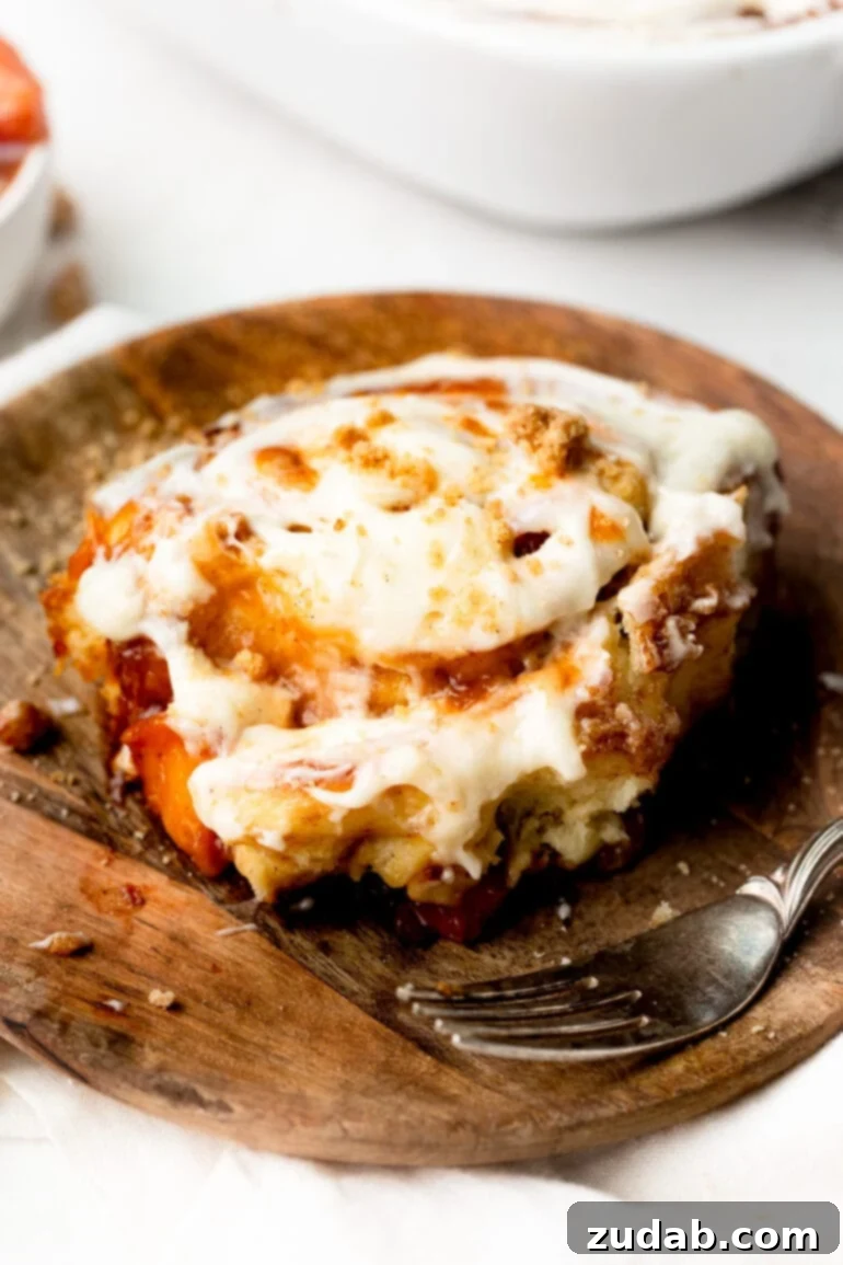 Delicious Peach Cobbler Cinnamon Rolls 13 a photo of a single cinnamon roll sitting on a small wooden dessert plate