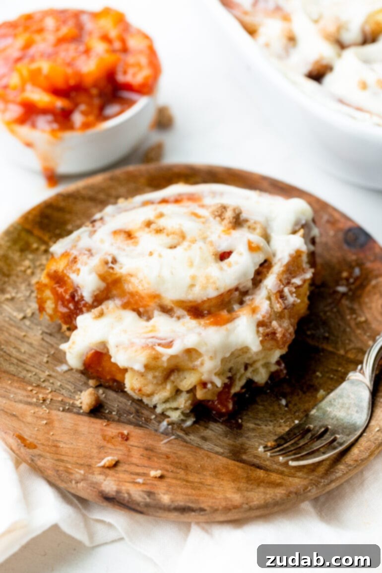 Delicious Peach Cobbler Cinnamon Rolls 5 a photo of a single baked cinnamon roll sitting on a wooden dessert plate with a fork sitting next to it