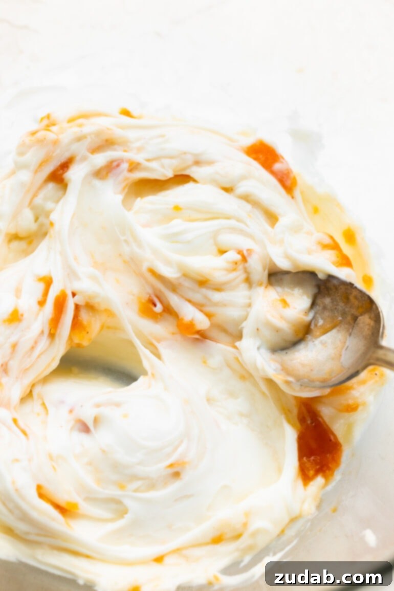Delicious Peach Cobbler Cinnamon Rolls 10 a photo of a golden baked cinnamon roll being topped with creamy white cream cheese frosting
