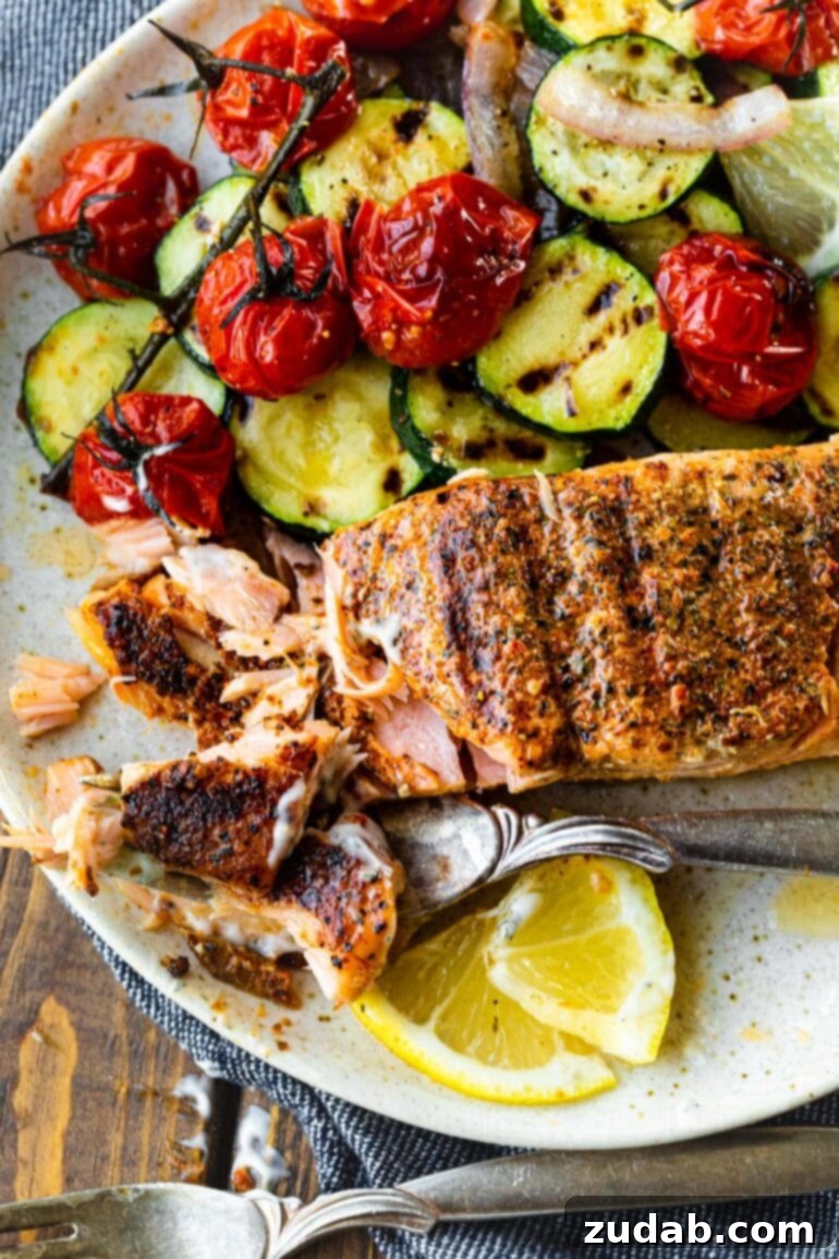 The Ultimate Guide to Perfectly Grilled Salmon 2 A perfectly grilled salmon fillet, flaked on one end, served alongside a medley of grilled vegetables and fresh lemon slices. This image highlights the crisp exterior and moist interior of the salmon, making it a healthy and visually appealing meal.