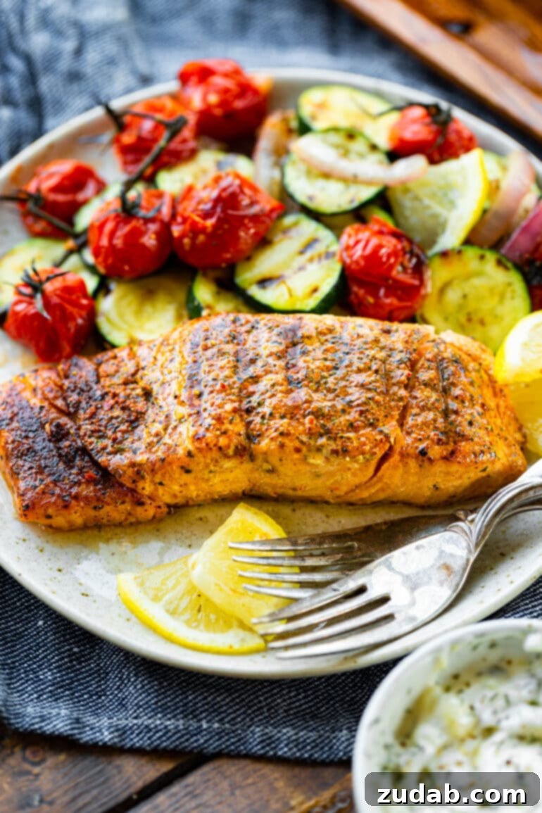 The Ultimate Guide to Perfectly Grilled Salmon 5 A succulent grilled salmon fillet, flaked to reveal its moist texture, artfully plated with tender grilled zucchini and vibrant cherry tomatoes. This image captures a healthy, protein-rich, and low-carb meal.