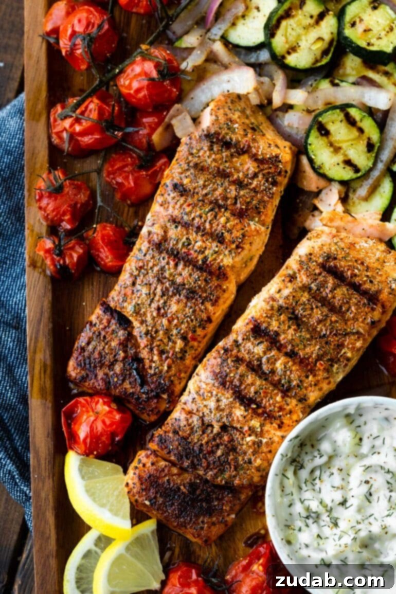 The Ultimate Guide to Perfectly Grilled Salmon 7 A rustic wooden serving tray holds two grilled salmon fillets, a small bowl of homemade tartar sauce, and a colorful array of grilled zucchini and cherry tomatoes, embodying a perfect summer meal.
