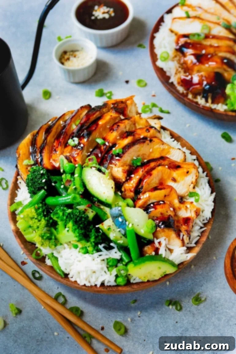 A photo of a plate of fluffy white rice covered with succulent teriyaki chicken and vibrant steamed broccoli and zucchini, showcasing a healthy and delicious meal.