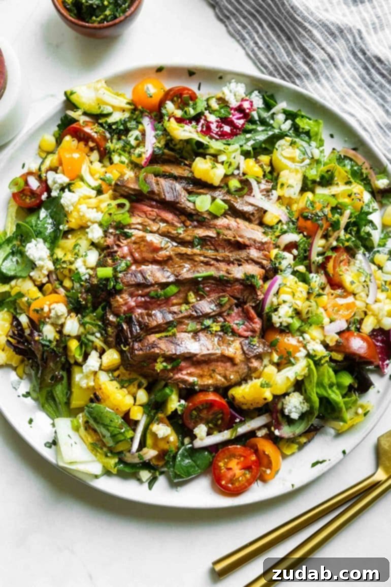 A photo of a large white plate full of a perfectly grilled steak and gorgonzola salad topped with vibrant grilled corn and crumbled gorgonzola cheese, offering a gourmet visual.