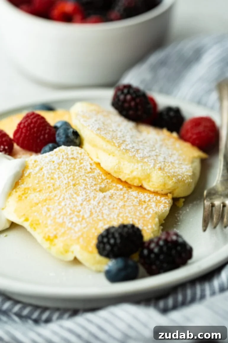 Pillowy Soft Japanese Pancakes 2 A photo of three fluffy Japanese cloud pancakes topped with powdered sugar and mixed fresh berries, ready to be enjoyed.