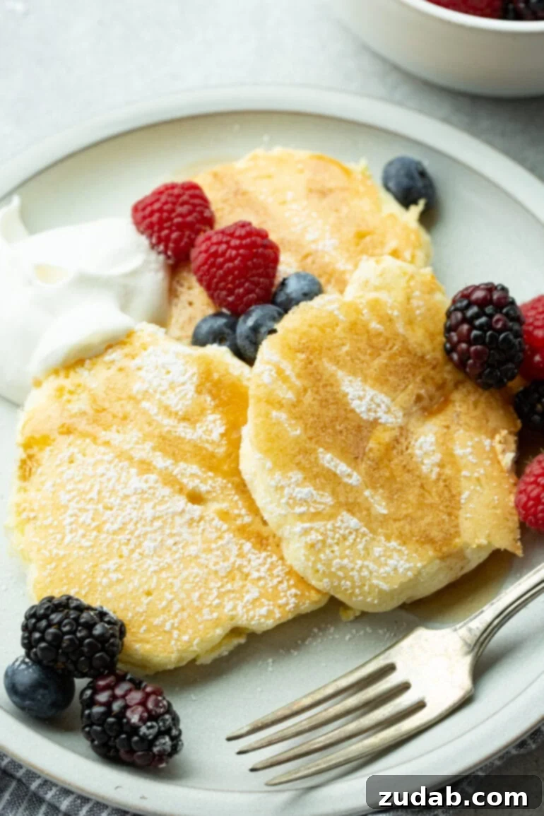 Pillowy Soft Japanese Pancakes 3 A photo of a plate full of fluffy Japanese cloud pancakes topped with powdered sugar, syrup, and a medley of fresh berries, a delightful breakfast.