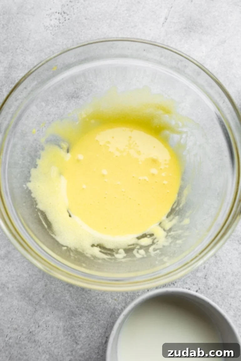 Pillowy Soft Japanese Pancakes 5 A photo of the egg yolk mixture for Japanese cloud pancakes in a large glass bowl, showing its pale and frothy texture.