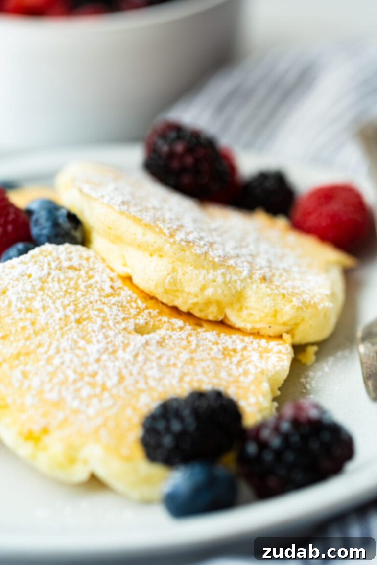 Pillowy Soft Japanese Pancakes 8 A photo of three fluffy golden Japanese cloud pancakes on a plate, generously topped with powdered sugar and mixed fresh berries.