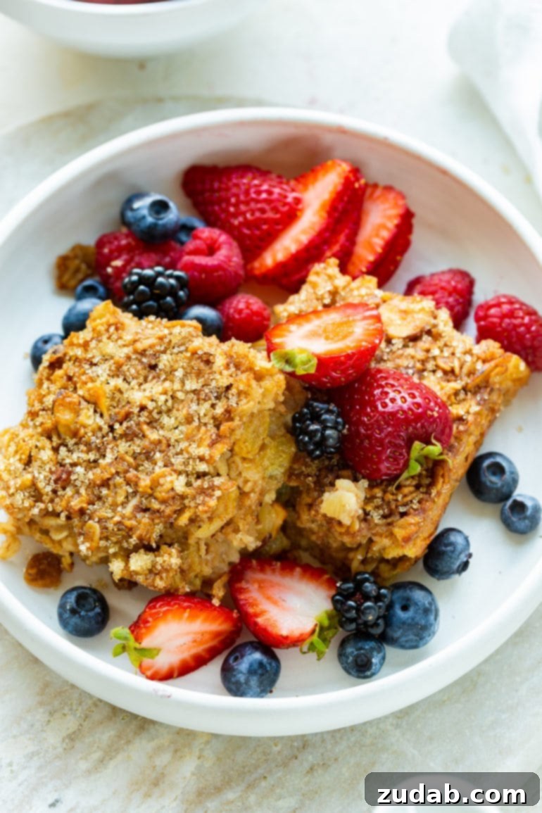 Weekly Meal Plan October 30 to November 5 7 Two generous slices of Creme Brulee Baked Oatmeal artfully arranged in a white bowl, surrounded by a vibrant mix of fresh berries, ready for a delightful breakfast.
