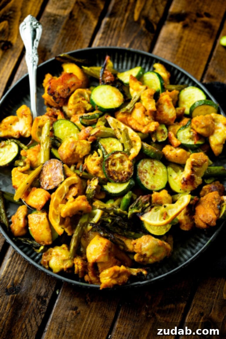 A dinner plate filled with bright orange-yellow bites of honey turmeric chicken mixed with perfectly roasted asparagus and zucchini.