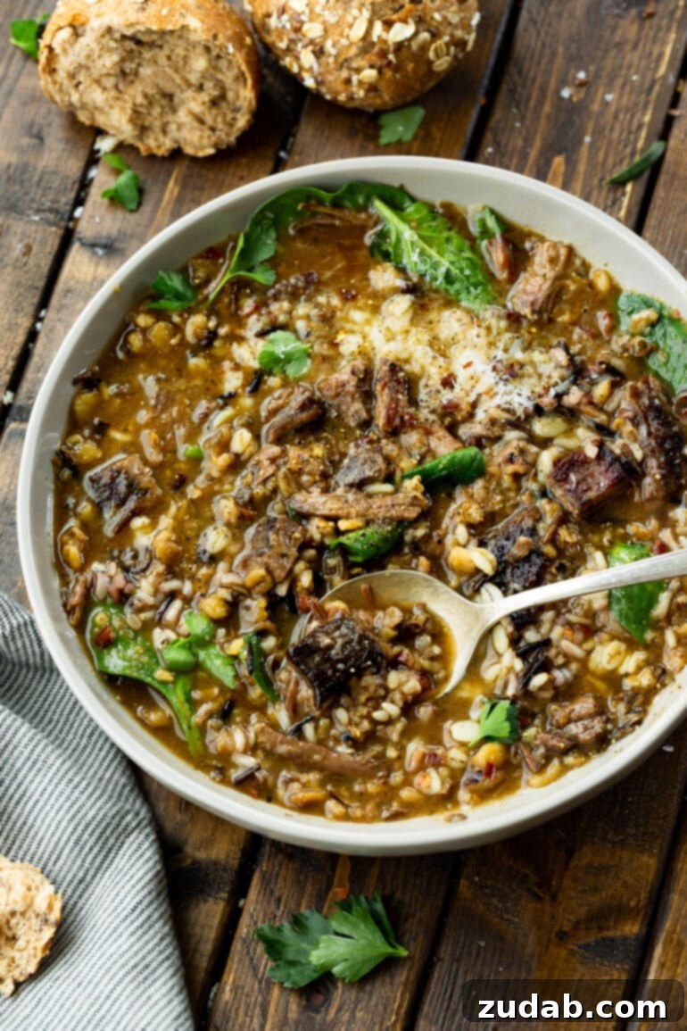 A comforting photo of a bowl filled to the brim with hearty beef barley soup, featuring tender beef chunks, mushrooms, barley, wild rice, and fresh spinach.