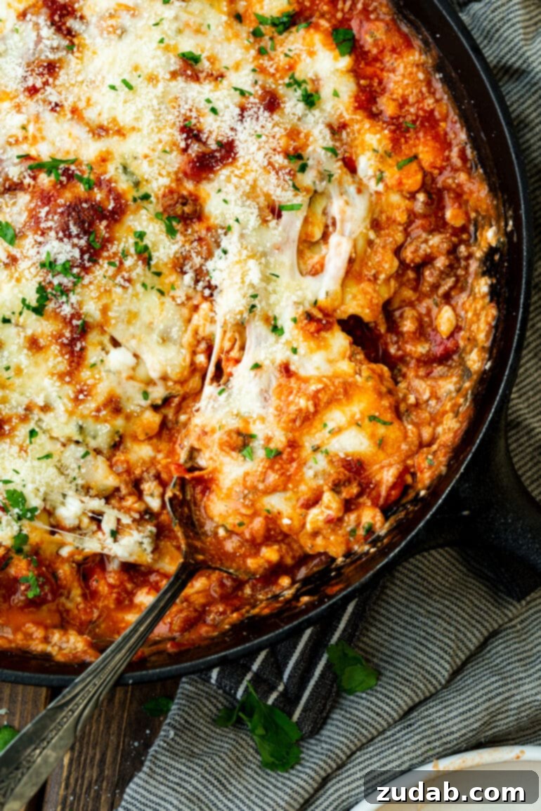 Effortless Skillet Ravioli Lasagna 2 A vibrant photo of a serving of skillet lasagna being scooped out of a sizzling cast iron skillet, showcasing layers of tender ravioli, savory meat sauce, and melted cheese.