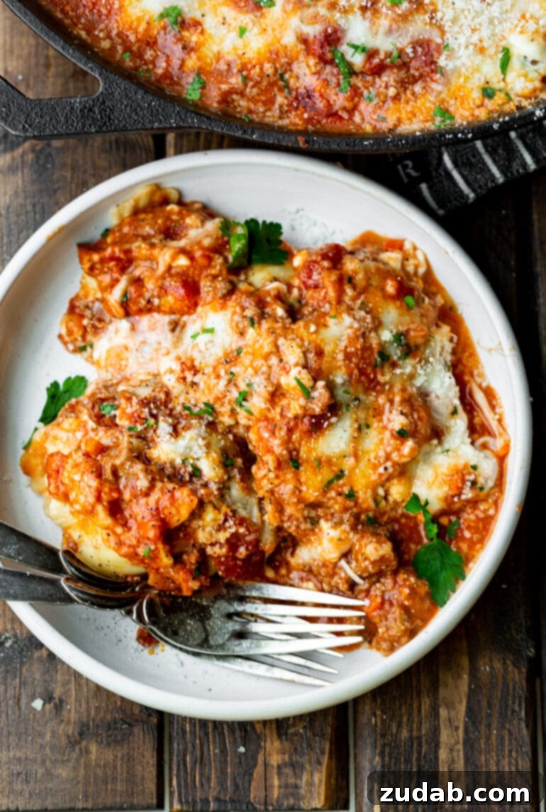 Effortless Skillet Ravioli Lasagna 3 A close-up photo of a generous serving of ravioli lasagna on a clean white dinner plate, accompanied by two forks, ready to be enjoyed.