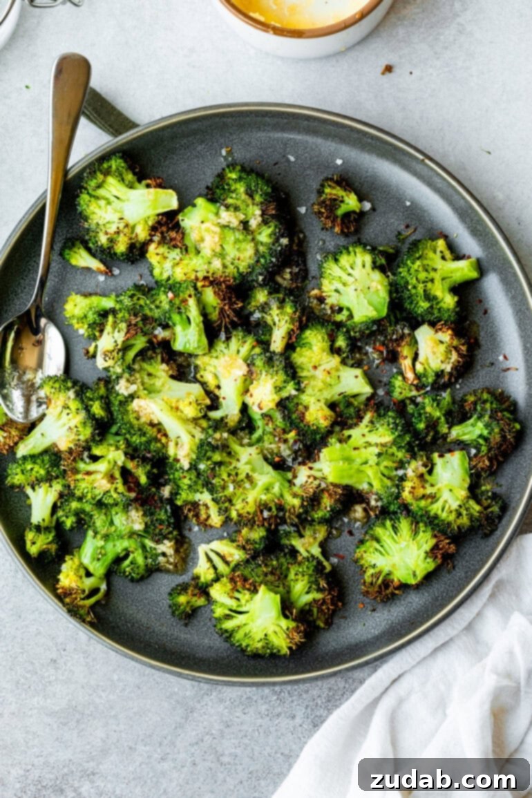 Golden Crispy Air Fryer Smashed Broccoli 4 A close-up, top-down view of smashed crispy air fried broccoli florets artfully arranged on a dark gray serving plate. The texture is prominent, highlighting the dish's ease and deliciousness as a healthy air fryer snack or side.