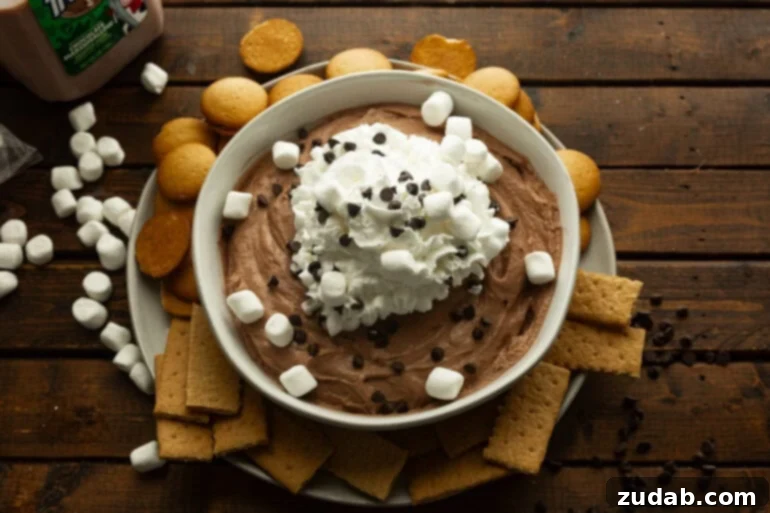 Festive Holiday Hot Chocolate Dip 2 A large bowl of creamy chocolate dip topped with mini marshmallows and mini chocolate chips, surrounded by graham crackers and Nilla wafers.