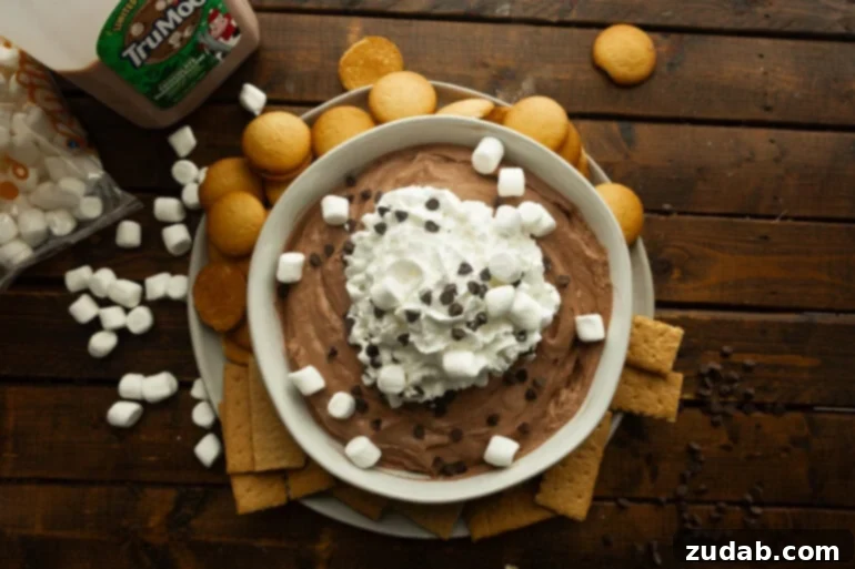 Festive Holiday Hot Chocolate Dip 4 A large bowl of creamy chocolate dip topped with whipped cream, mini marshmallows, and mini chocolate chips, with Nilla wafers and graham crackers.