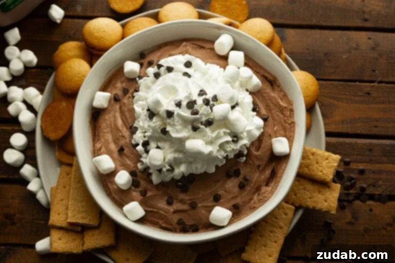 Festive Holiday Hot Chocolate Dip 5 Creamy hot cocoa dip in a large white bowl topped with whipped cream, mini marshmallows, and mini chocolate chips.