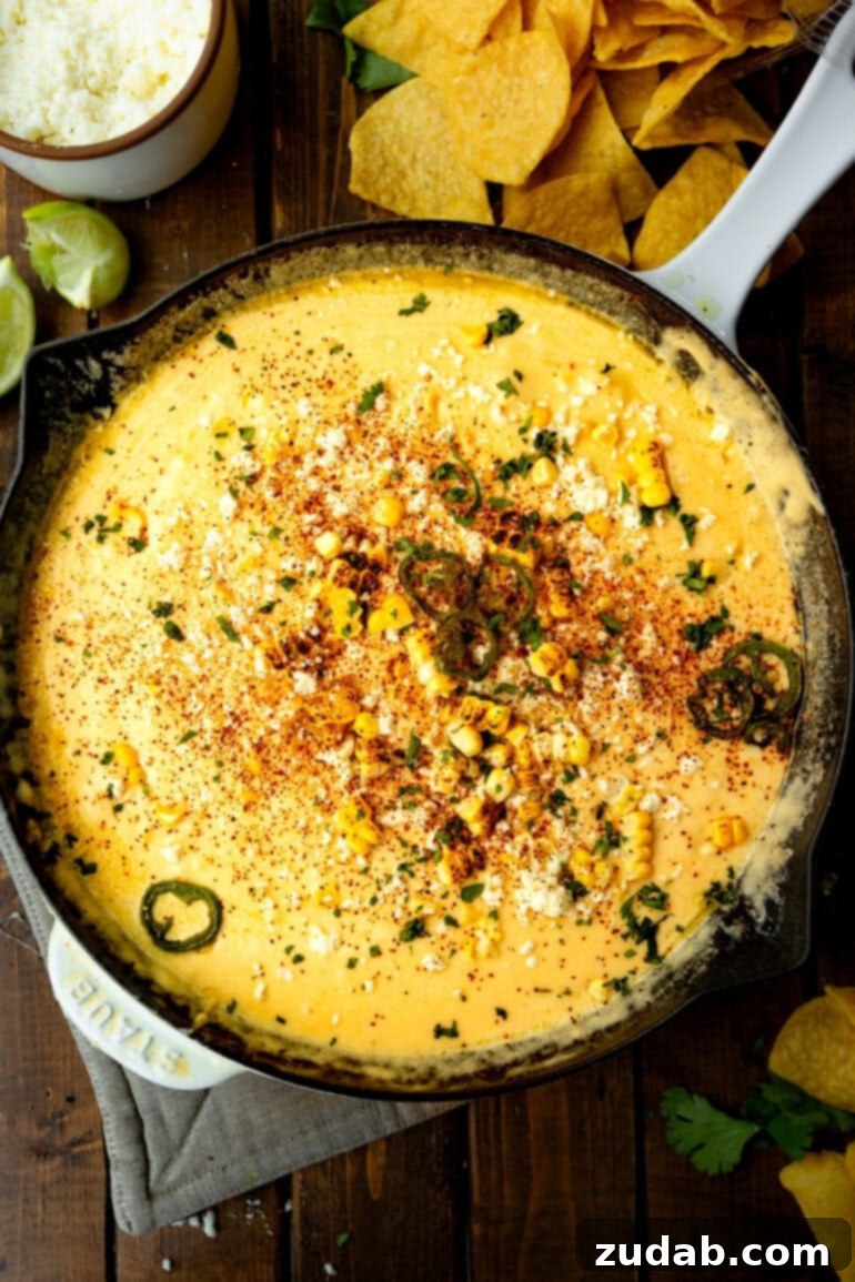 Elote-Inspired Queso Dip 5 street corn queso dip bubbling and served in a skillet with fresh cilantro, crema, and tortilla chips on the side.