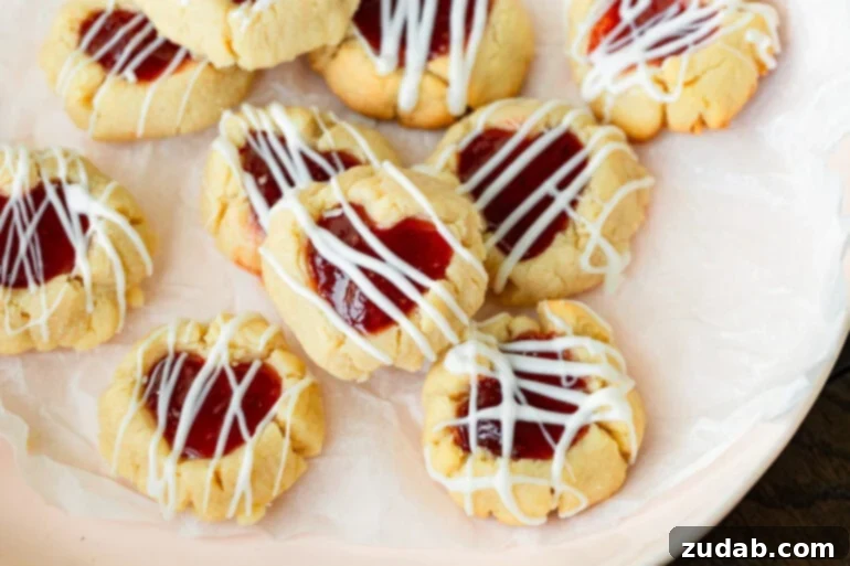 Valentine's Day Thumbprint Cookies: A Sweet Treat for Your Loved Ones 3 Valentine’s Day thumbprint cookies arranged on a plate with jam-filled centers and white chocolate drizzle.