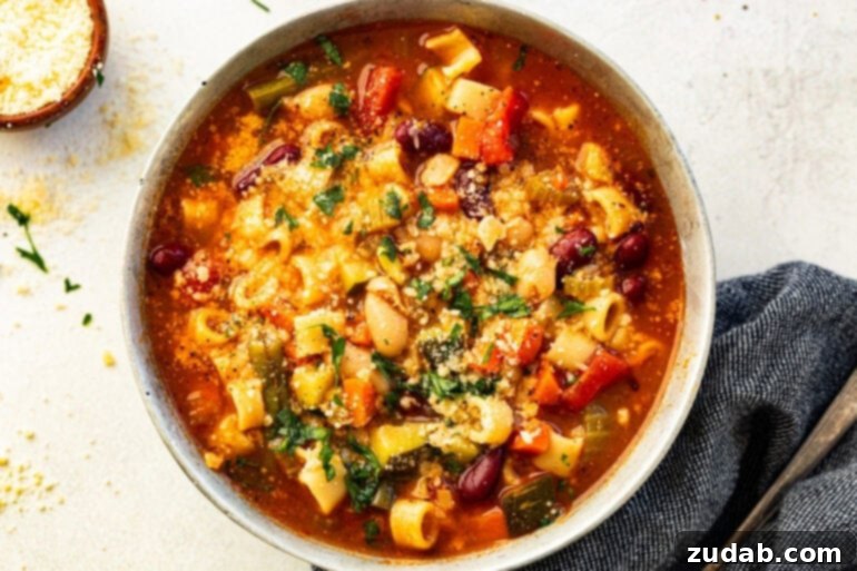 Grandma's Secret Garden Minestrone 6 A close-up of hearty Italian vegetable and bean soup in a white ceramic bowl, showcasing the rich broth and vibrant mix of vegetables.
