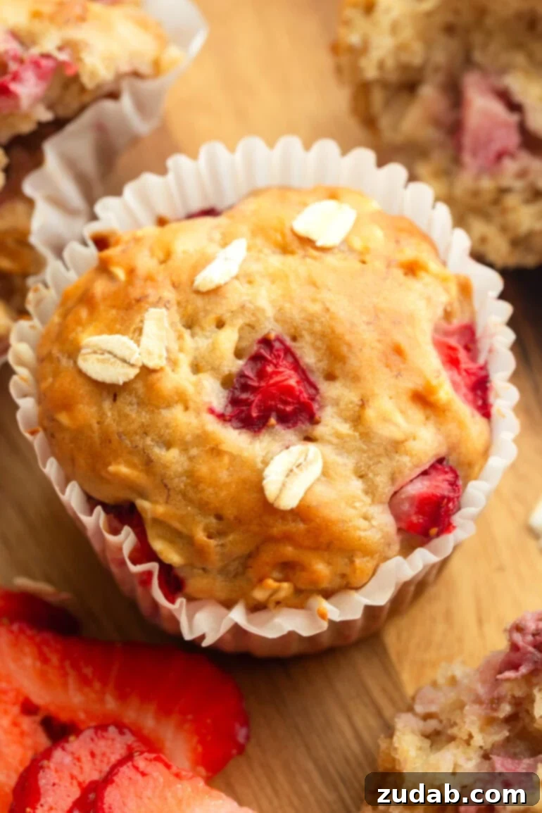 Super Soft Strawberry Oat Muffins Infused with Greek Yogurt 7 A single, perfectly baked healthy strawberry oat muffin with a golden-brown top, sitting on a wire rack, ready to be eaten.