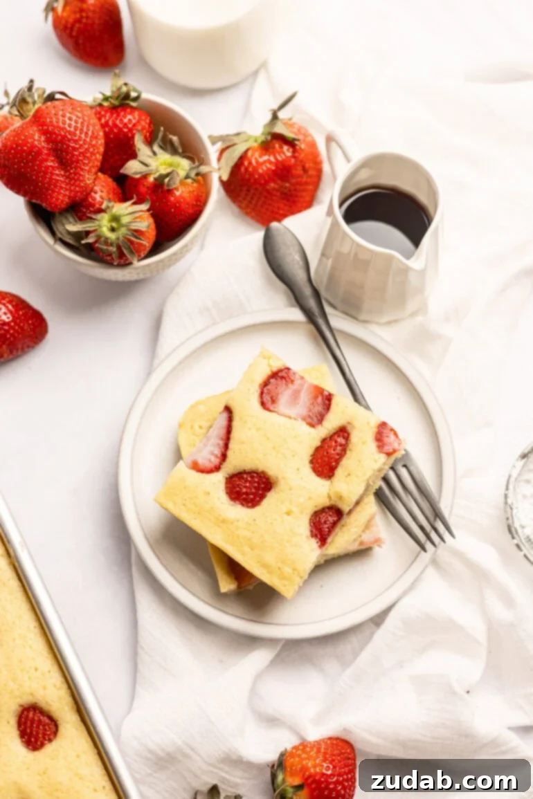 Sheet Pan Strawberry Pancake Bake 5 Two generous slices of strawberry sheet pan pancakes, perfectly stacked on a pristine white plate, with a fork poised beside them. A truly inviting breakfast scene.