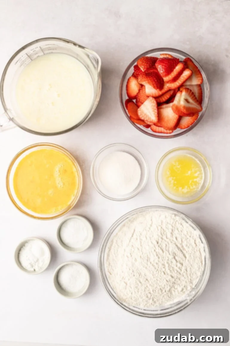 Sheet Pan Strawberry Pancake Bake 6 All the fresh ingredients for making strawberry sheet pan pancakes, neatly arranged in separate small glass bowls. Visible are flour, creamy buttermilk, granulated sugar, fresh eggs, baking powder, baking soda, melted butter, and perfectly sliced bright red strawberries.